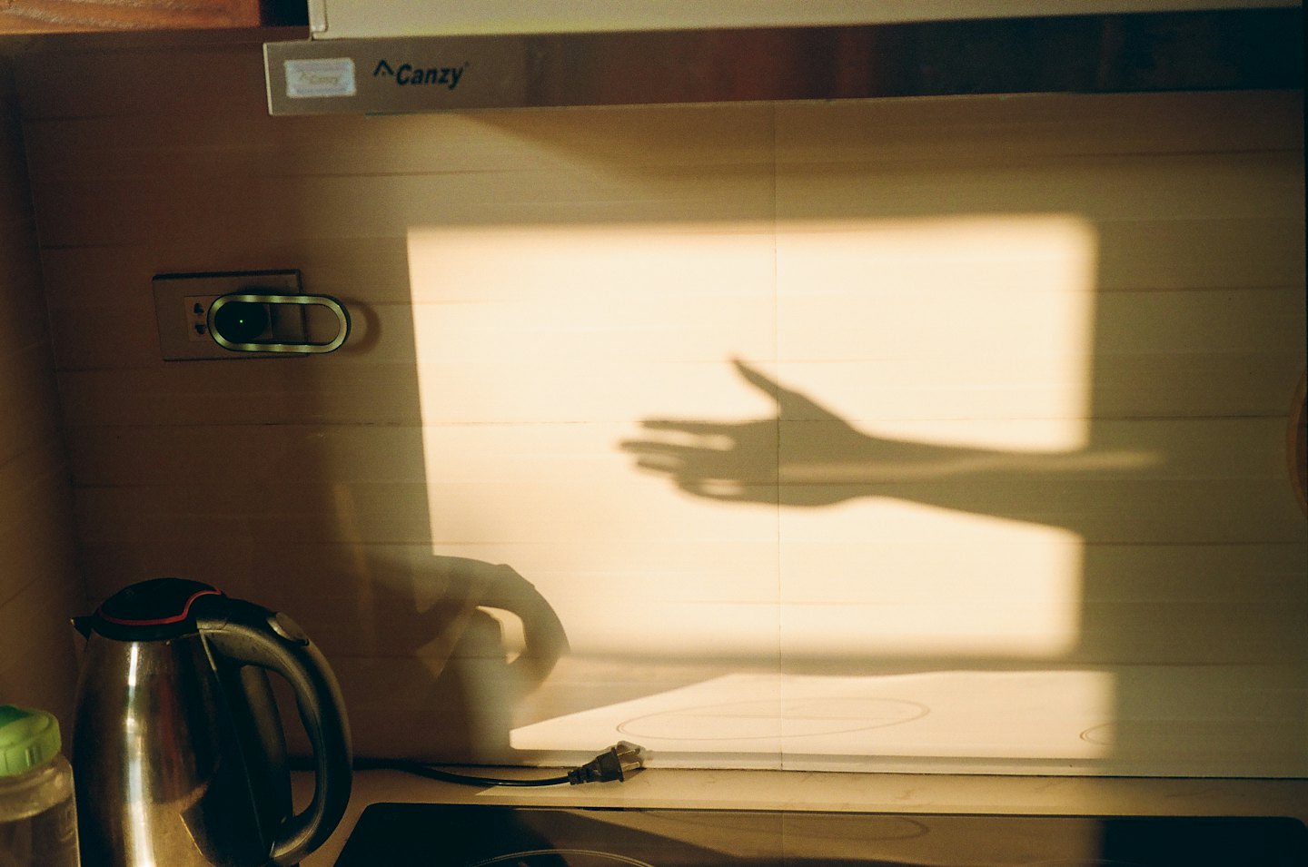 Hand shadow gesture on a wooden kitchen wall near an electric kettle.
