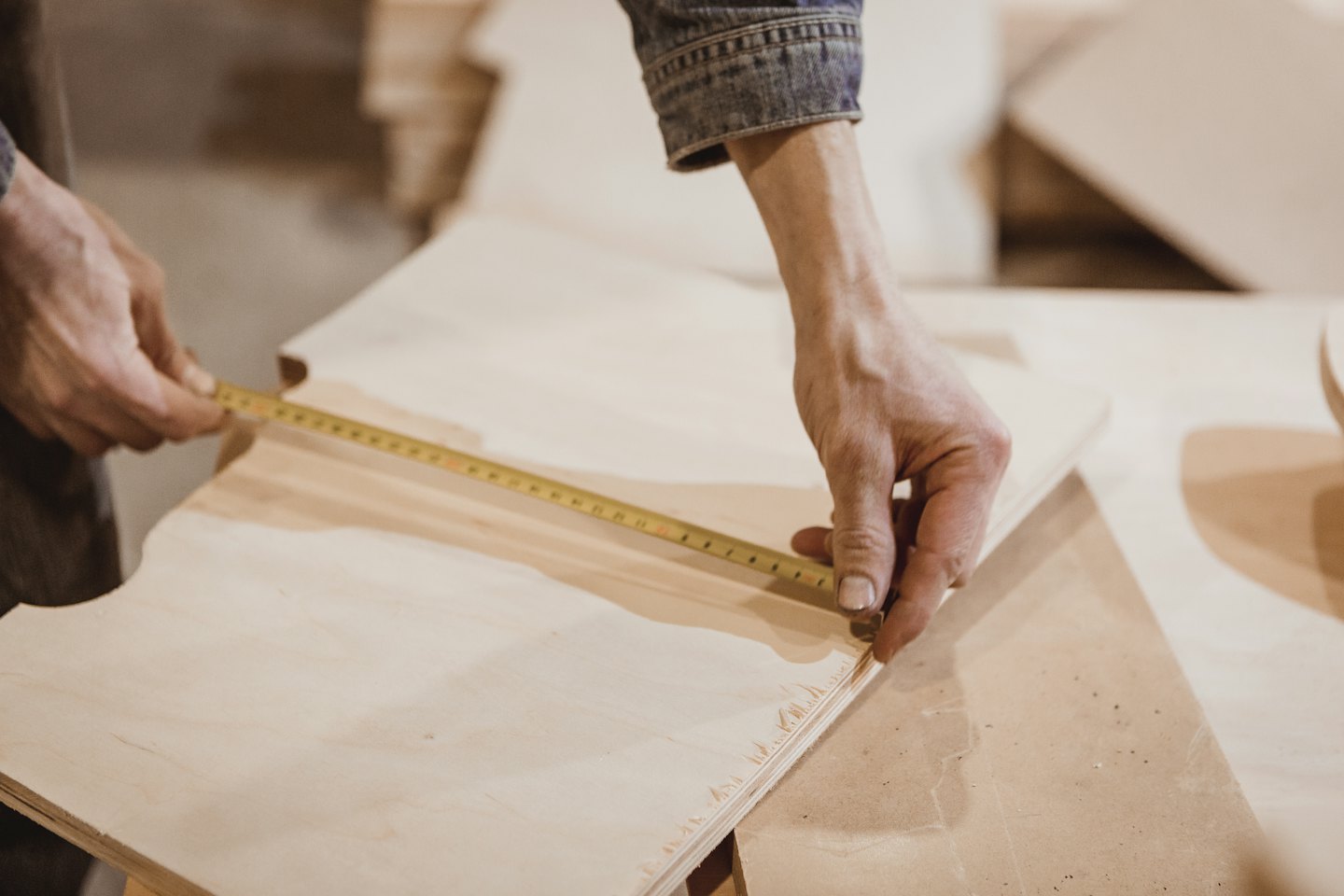 Hands measure plywood with a yellow tape measure.
