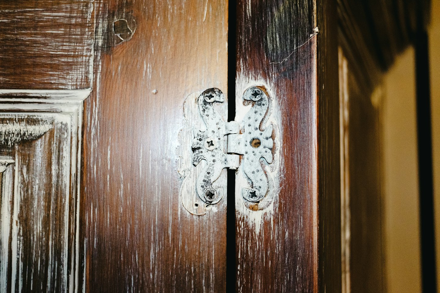 Distressed grey metal hinge attached to dark wooden cabinet doors.